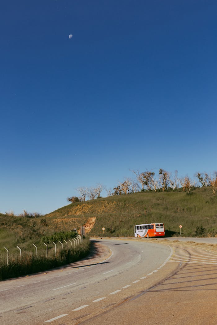 A picturesque road in Minas Gerais, Brazil, with a bus under a clear blue sky and visible moon.